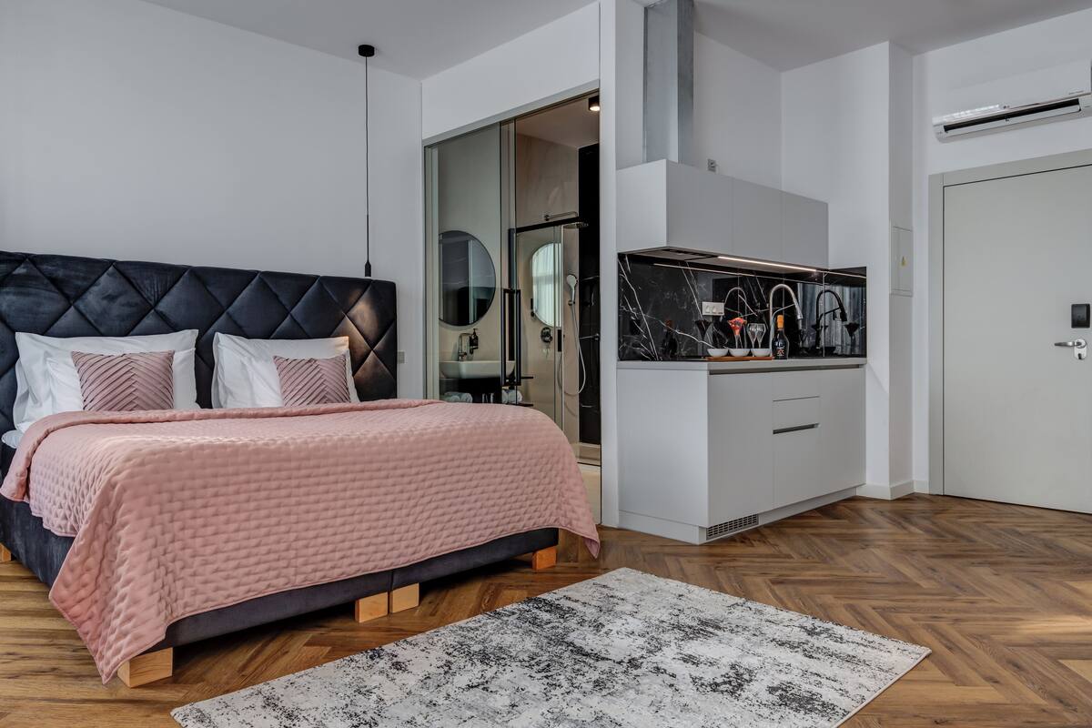 A modern bedroom with a bed, bedside tables, a mirror, and a bathroom with a sink and shower.