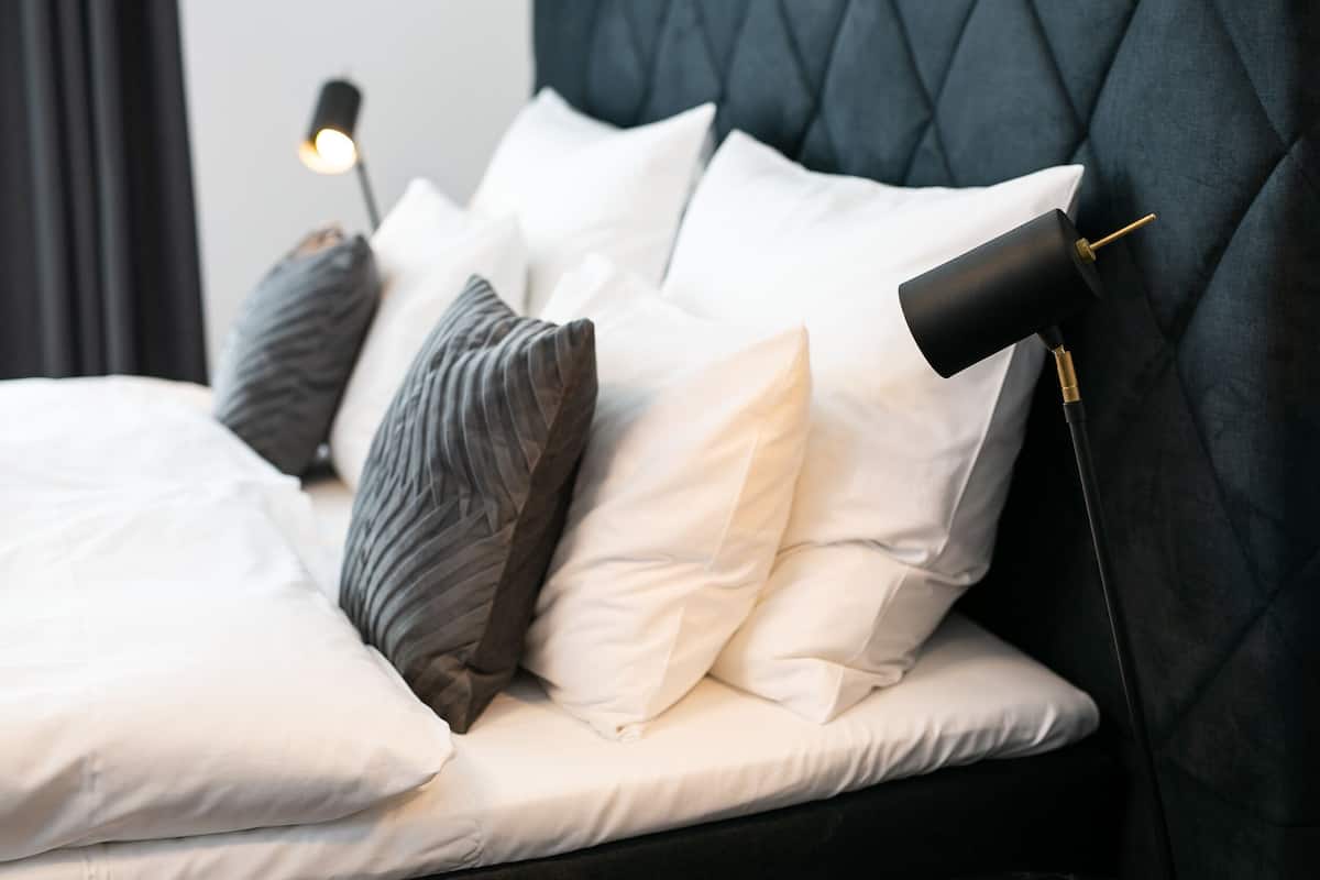 A neatly made bed with white and gray pillows, a black headboard, and a bedside lamp.