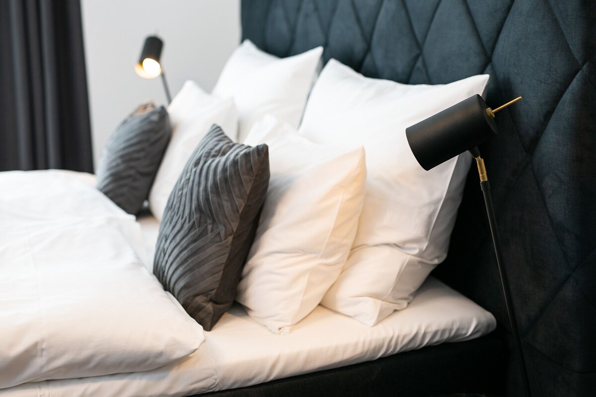 A neatly made bed with white and gray pillows, a black headboard, and a bedside lamp.