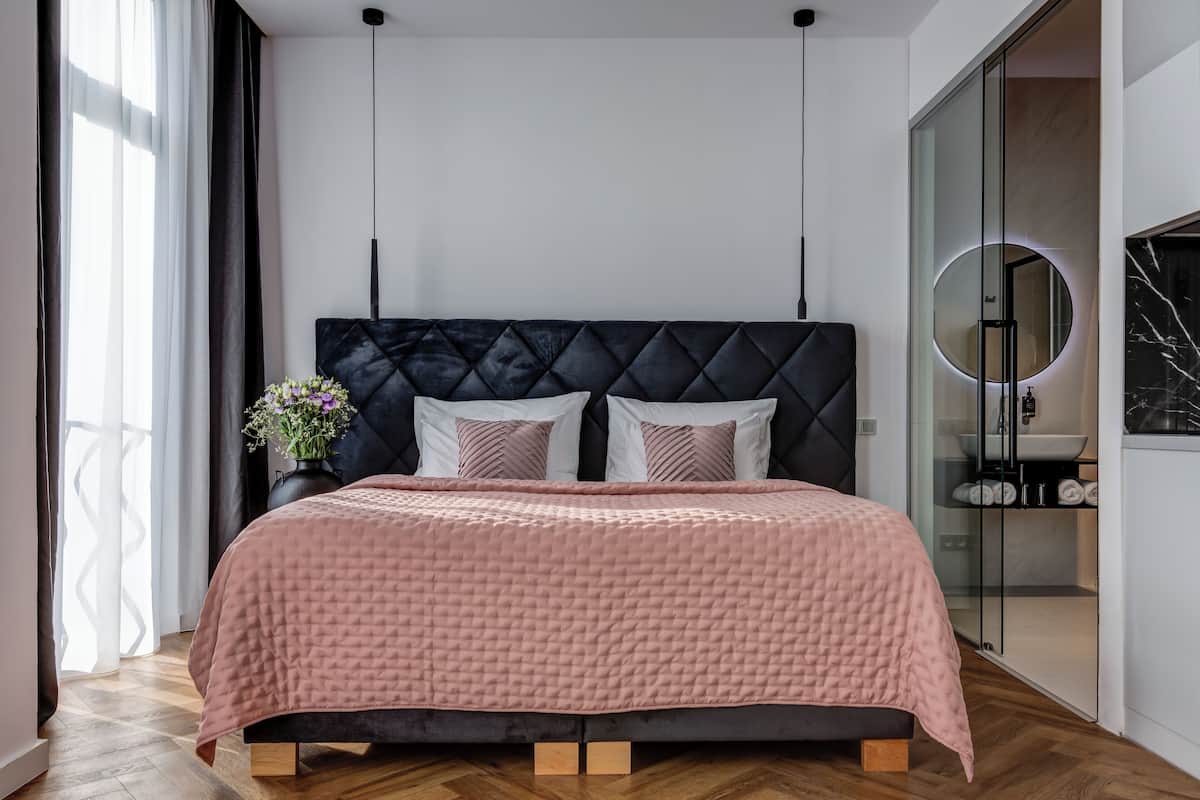 A modern bedroom with a large bed, a dark headboard, and a bedside table with a vase of flowers.