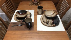 A dining table set with plates, bowls, a mug, and cutlery. - Halfway Tiny House - 3 BR Small Town Iowa Rural Setting! (Britt)