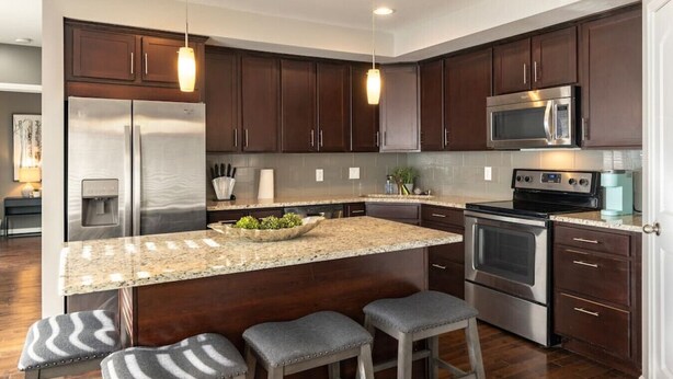 A modern kitchen with dark wood cabinets, stainless steel appliances, a granite countertop, and bar stools. - Stylish 2BR near it all (Cincinnati)