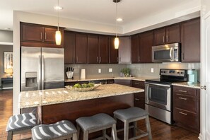 A modern kitchen with dark wood cabinets, stainless steel appliances, a granite countertop, and bar stools. - Stylish 2BR near it all (Cincinnati)
