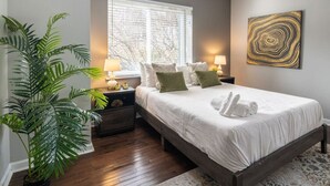 Een slaapkamer met een groot bed, twee nachtkastjes met lampen, een potplant en een raam met zonwering.