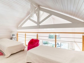 Amplia habitación con techo alto y vigas de madera, con dos camas con ropa de cama blanca y una silla roja brillante.