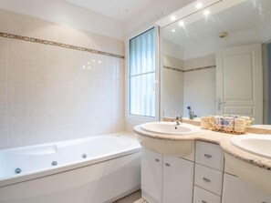 Ein modernes Badezimmer mit einer Badewanne, zwei Waschbecken, einem großen Spiegel und einem Fenster.
