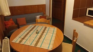 Ein gemütliches Zimmer mit einem Holzkopfteil, einem runden Tisch mit karierter Tischdecke, einer kleinen Vase und einem Holzstuhl.
