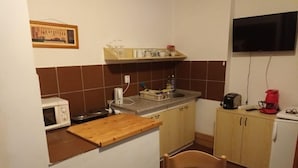 Eine kompakte Küche mit Mikrowelle, Schneidebrett aus Holz, Spüle und kleinem Kühlschrank.