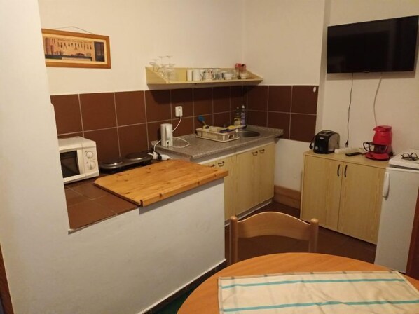 A compact kitchen with a microwave, a wooden cutting board, a sink, and a small refrigerator.