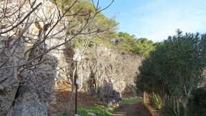 Ein schmaler, gepflasterter Weg, gesäumt von felsigem Gelände und vereinzelter Vegetation, der zu einer Klippe führt.