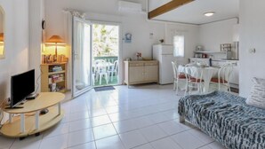 Ein kompakter Wohnbereich mit Fernseher, Bücherregal, Essbereich, Küchenzeile und einem Balkon mit Sitzgelegenheiten.