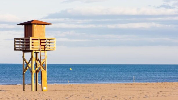 Ein hölzerner Rettungsschwimmturm am Strand unter einem wolkenlosen Himmel.