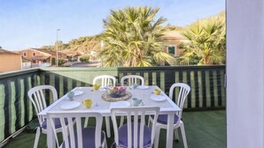 Ein Balkon mit einem Tisch für vier Personen, umgeben von weißen Stühlen mit violetten Kissen.