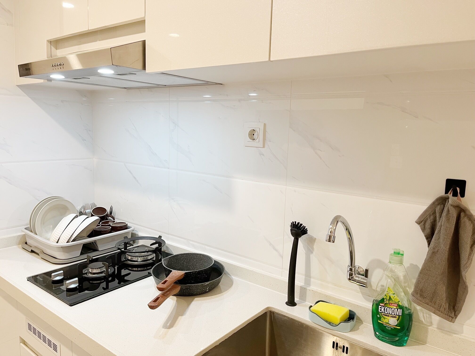 A kitchen with white marble tiles, a stove, a sink, and various kitchen items.