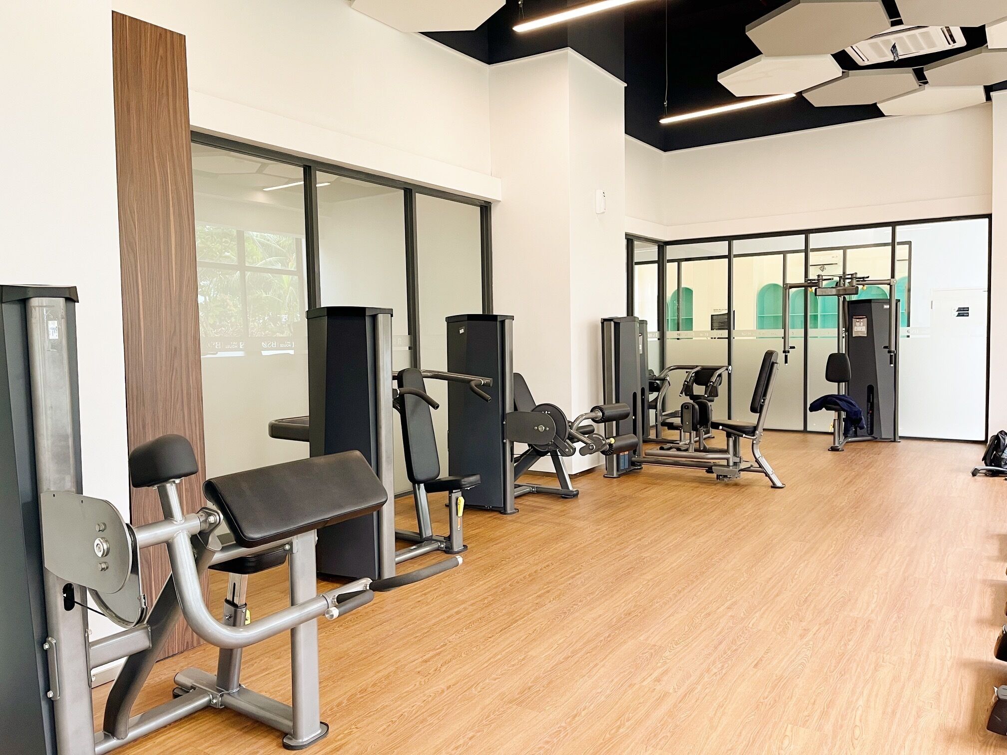 A gym with various exercise machines, wooden flooring, and large windows.