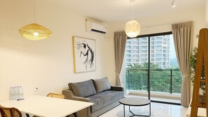 Un saló modern amb un sofà, taula de menjador, cadires i una taula rodona petita. Hi ha una finestra gran amb cortines, un aparell d'aire condicionat i un quadre a la paret.