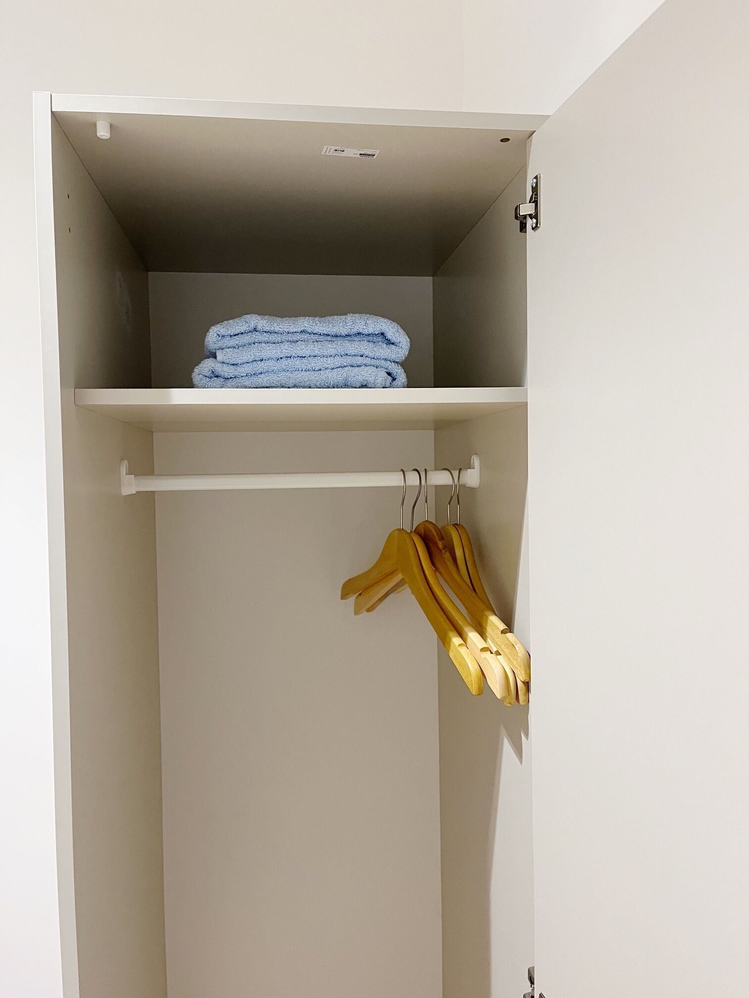 A closet with a shelf holding folded towels and a rack with hangers.