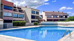 Une piscine entourée d’une terrasse carrelée, elle-même bordée d’immeubles à plusieurs étages dotés de balcons et de fenêtres.