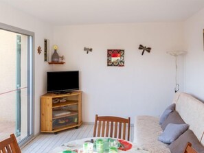 Uma sala de estar aconchegante com uma TV sobre um suporte de madeira, uma mesa de jantar com cadeiras e um sofá.
