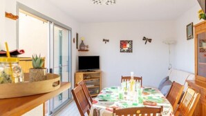 Un coin repas avec une table dressée pour quatre personnes, un téléviseur posé sur un meuble et une fenêtre donnant sur l’extérieur.