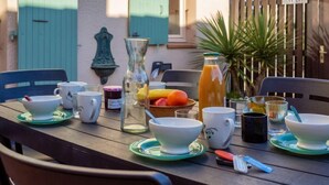 Une table en bois, mise avec des tasses et des soucoupes blanches, un pichet en verre, une bouteille de jus d’orange et un saladier rempli de fruits.