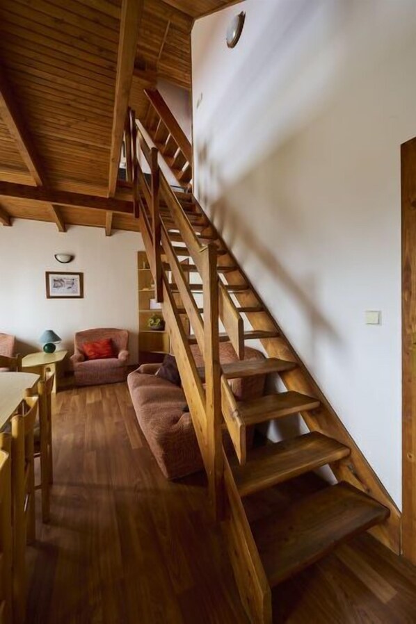 A wooden staircase leading to an upper level, a wooden dining table with chairs, and a cushioned seating area. - Mountain Duplex & Balcony by Interhome (Harrachov)