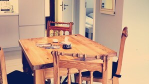 Een houten eettafel met vier stoelen, een rode hanglamp, een spiegel aan de muur en een deur die leidt naar een andere kamer.
