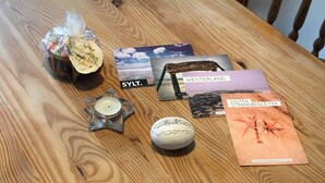 Een houten tafel met een kaars, een bord met 'Welkom' erop, een klein decoratief object en brochures.