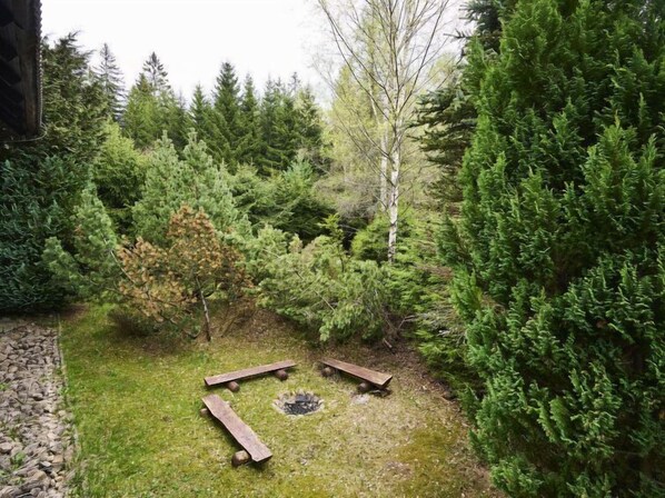 Un jardin agrémenté d’un foyer et de bancs en bois, le tout entouré d’une végétation luxuriante.