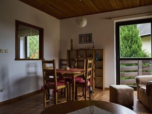 Een eethoek met een houten tafel en stoelen, een boekenkast en uitzicht op groen.