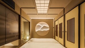 Una tradizionale stanza in stile giapponese con pavimento in tatami, un letto basso, porte scorrevoli e un elemento decorativo circolare a parete.