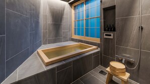 Un bagno moderno con una vasca da bagno in legno, una finestra con vetri azzurri e uno spazio doccia.