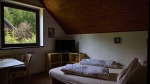 Una habitación acogedora con techo de madera, un ventanal grande, cama, televisor y una mesita.