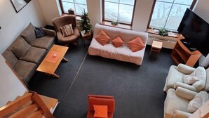 Uma sala de estar moderna com um sofá castanho, um sofá branco, um sofá vermelho e uma poltrona branca. Há uma pequena mesa de madeira e uma TV sobre um móvel.