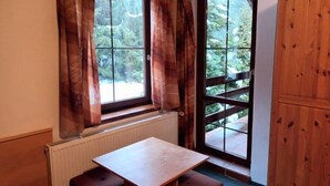 Quarto com mesa e banco de madeira, radiador e janela com cortinas.