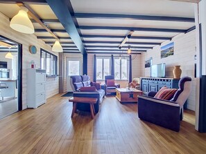 A spacious living area with wooden floors, a sofa, a chair, and a dining table. There are large windows allowing natural light and a view of the outdoors. - An Neizh by Interhome (Locquirec)