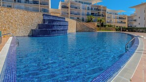 A swimming pool with a stone wall and steps leading into it, surrounded by modern buildings with balconies. - Vista Mar by Interhome (Albufeira)