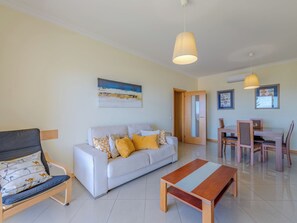 Una sala de estar con un sofá, una mesa de centro de madera, un comedor con mesa y sillas, y una puerta que da a otra habitación.