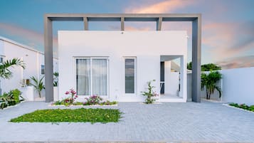 Simple, modern home with a flat roof, large windows, and a clean facade, set amidst a serene garden.