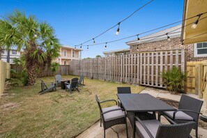 A backyard with a patio table and chairs, a wooden fence, and a palm tree. - Cozy PCB Beach House | Walk to the Beach! (Panama City)