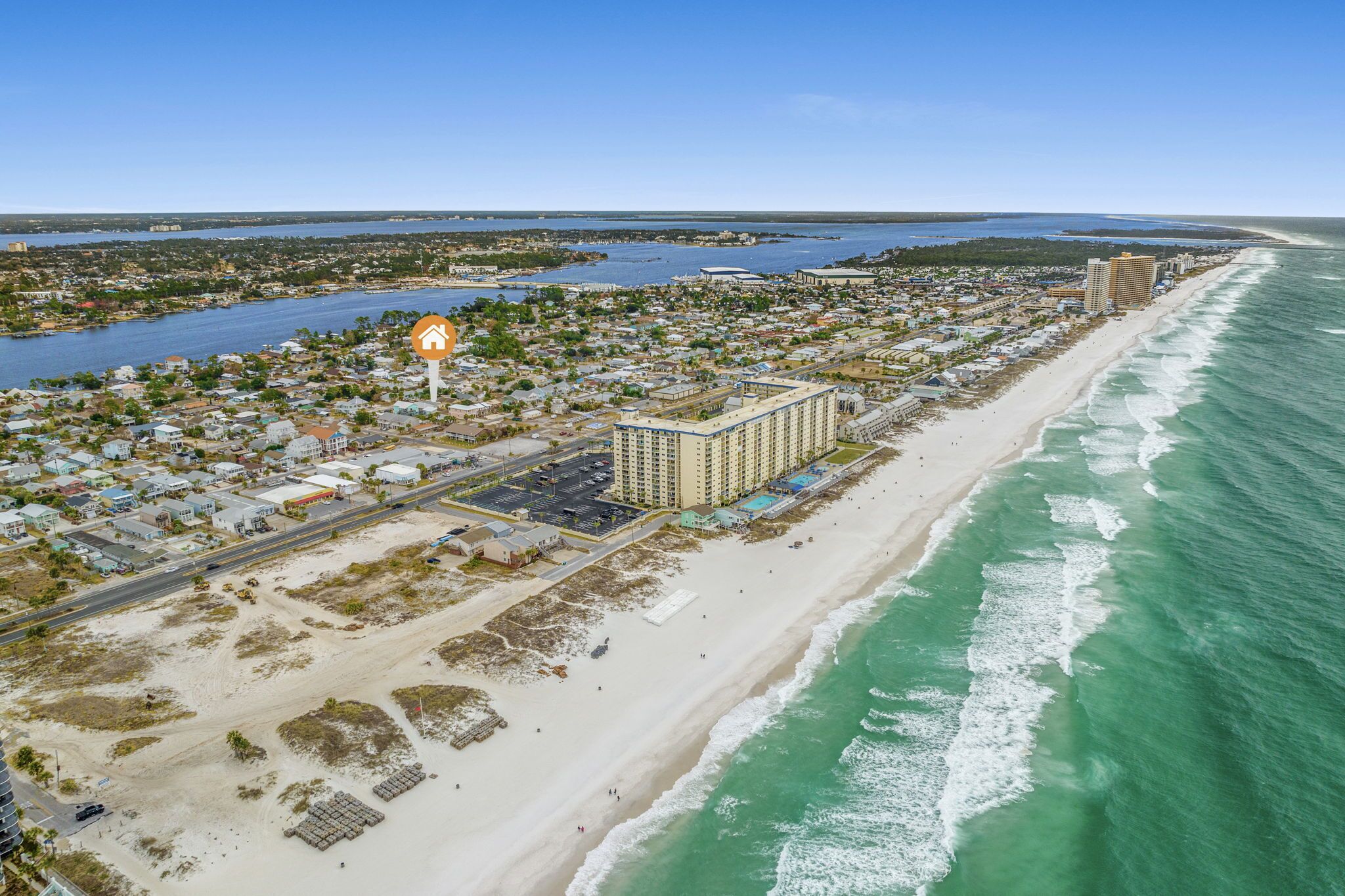 An aerial view of a coastal town with a beachfront hotel, a marina, and a road running parallel to the beach.