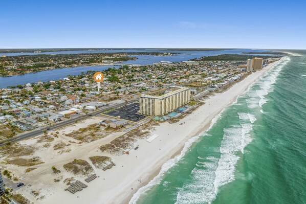 An aerial view of a coastal town with a beachfront hotel, a marina, and a road running parallel to the beach.