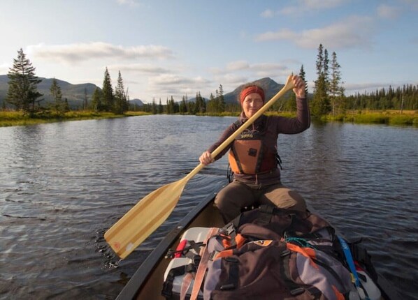 Une personne dans un canoë, sur une rivière bordée d’arbres et entourée de montagnes.