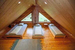 Een zolderkamer met een puntdak, drie eenpersoonsbedden, een raam en een houten vloer.