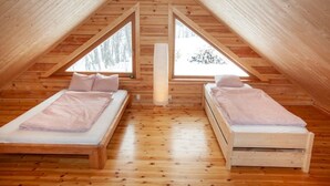 A cozy attic bedroom with two beds, wooden floors, and large windows.