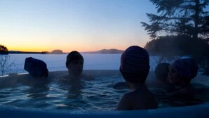 A hot tub with three people, surrounded by a natural landscape and trees.