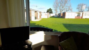 Een kamer met een televisie, een stoel en uitzicht op een gazon met een gebouw op de achtergrond.