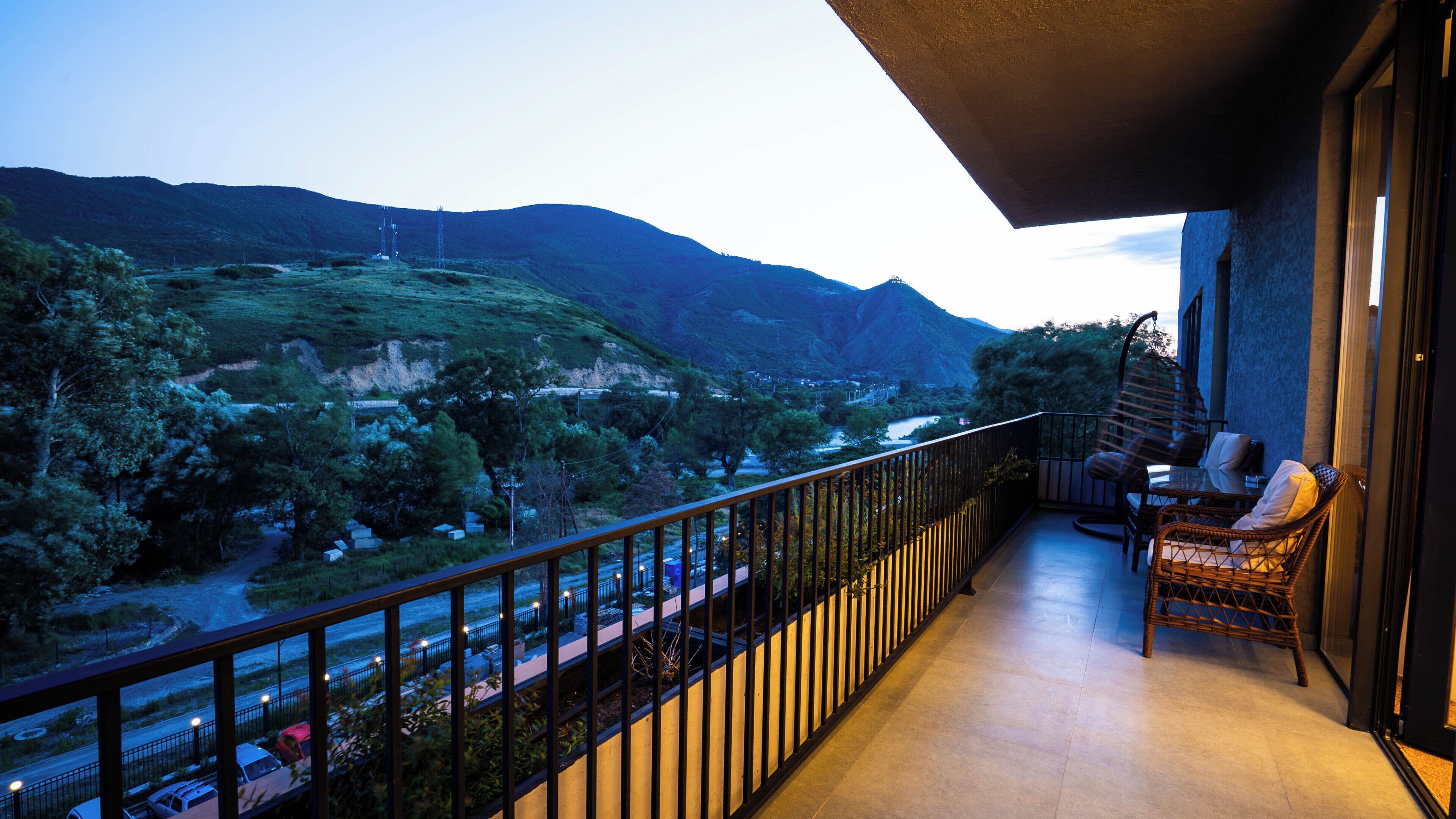 A balcony with a view of a valley and mountains, a wicker chair, and a glass table.