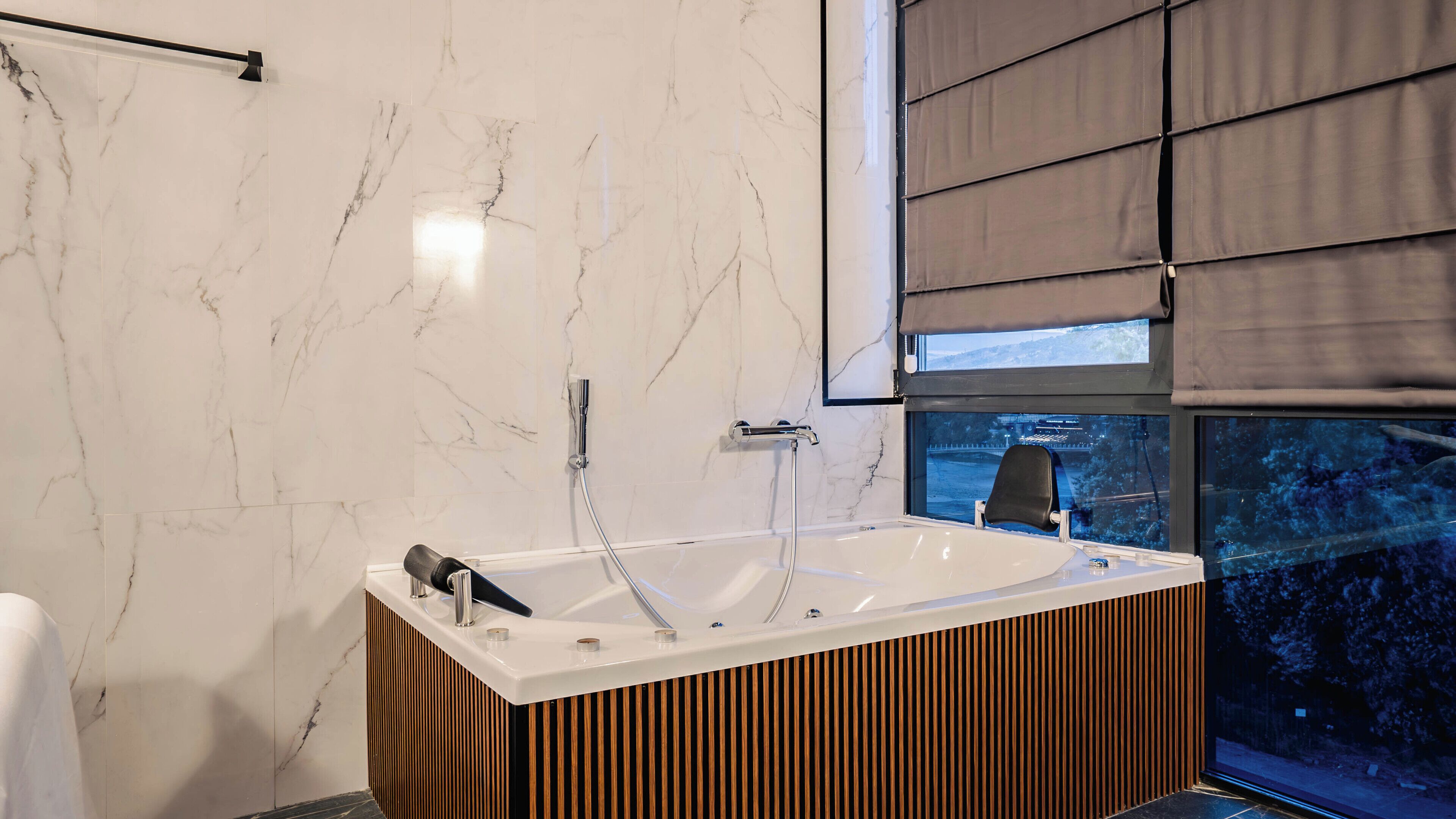 A modern bathroom with a marble wall, a bathtub, and a window with a view.