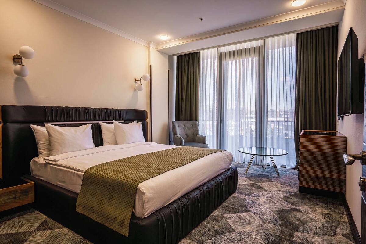 A hotel room with a large bed, a chair, a small table, and a TV.